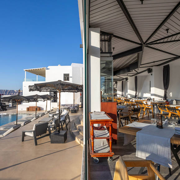 Dione restaurant's outdoor dining area and poolside view at Grand Ambassador in Santorini under clear blue sky